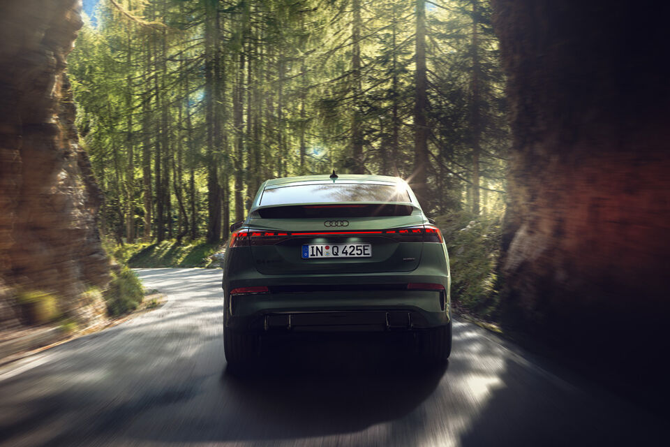Nieuwe Audi Q4 Sportback e-tron rijdend achter bos